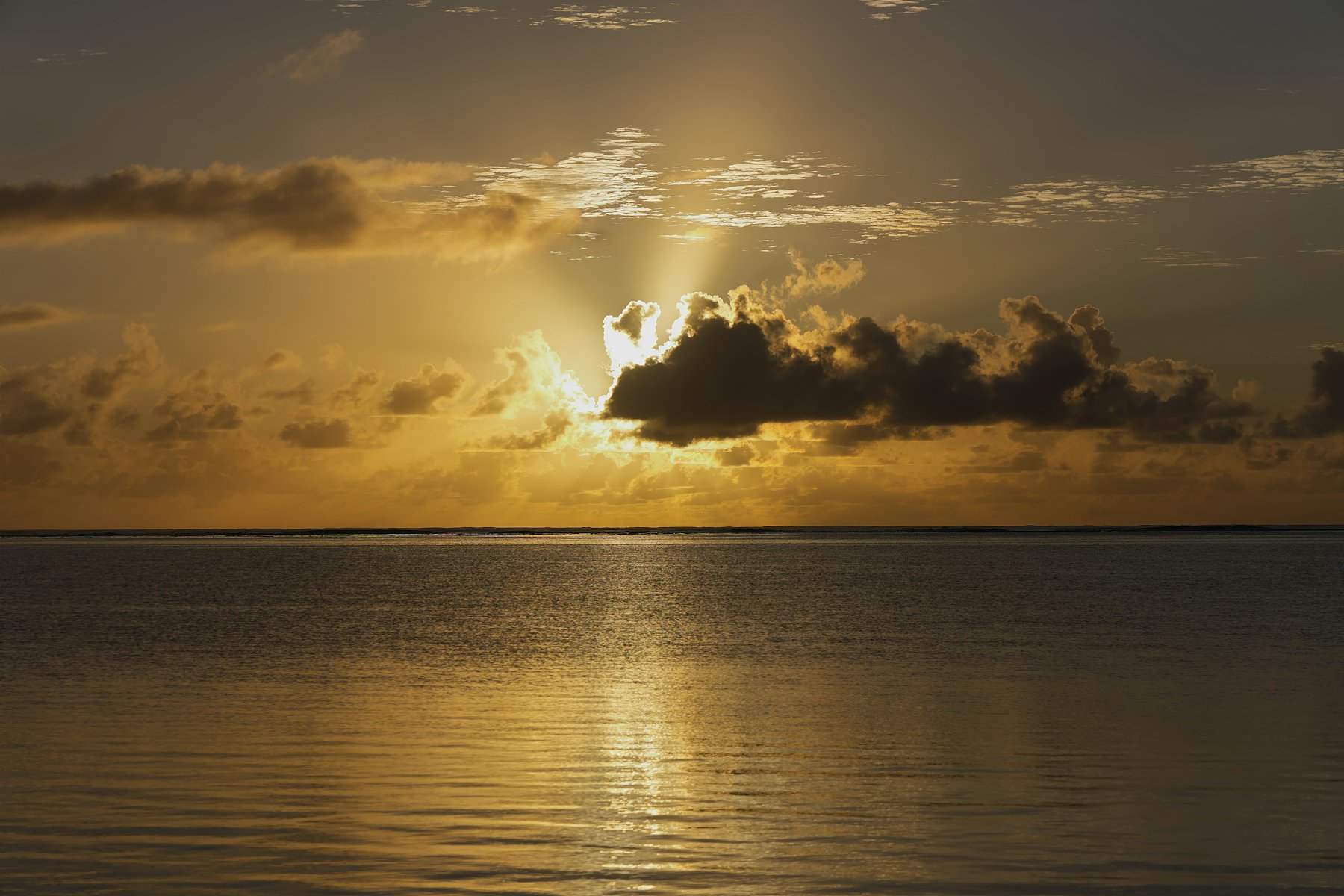 Sunlight breaking through clouds over calm golden water
